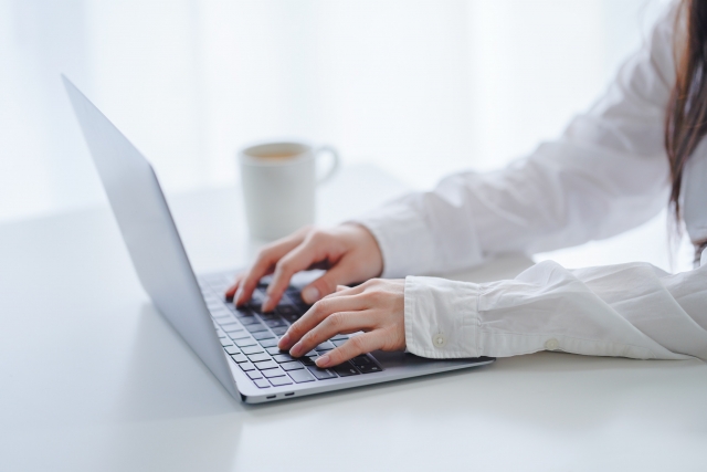 髪が長くて白い服を着た女性がパソコン作業をしている写真